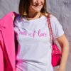 Mujer vistiendo camiseta blanca con letras en rosa fucsia en el pecho.