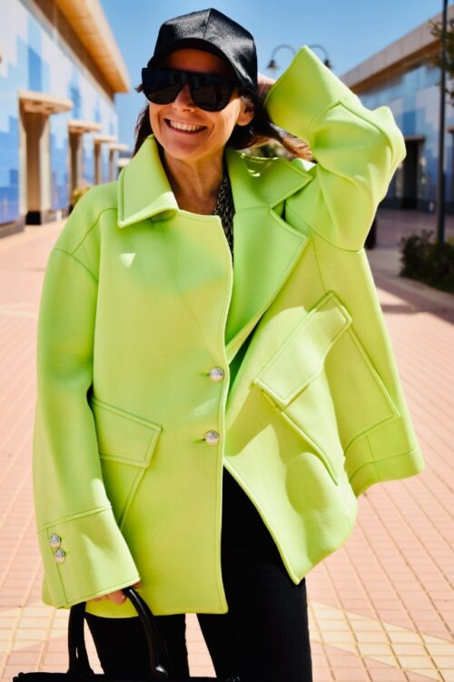 Mujer vistiendo abrigo oversize verde fluor, gorra negra y gafas de sol.