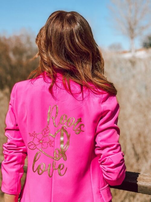 Mujer de espalda vistiendo blazer rosa fucsia con logo Roots of Love en la espalda,