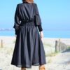 Mujer de espalda que lleva un vestido largo negro en la playa.