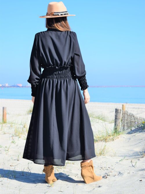 Mujer de espalda que lleva un vestido largo negro en la playa.